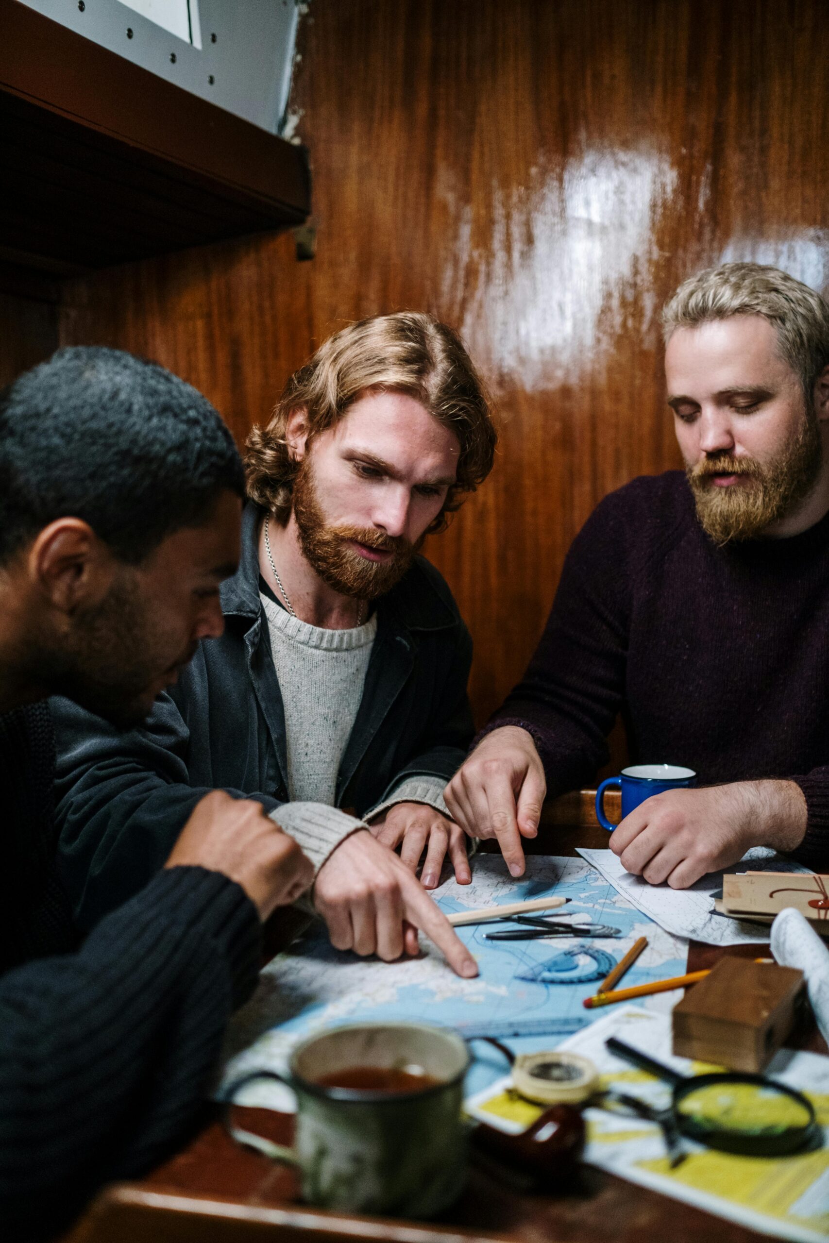 Three men planning a nautical journey using maps, indoors. Perfect for themes of adventure and teamwork.